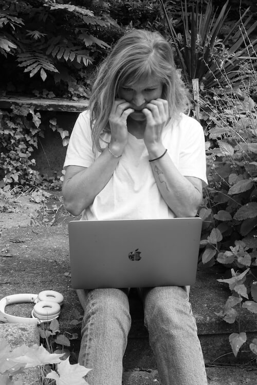 Eine blonde junge Frau schaut verzweifelt auf den Bildschirm ihren Laptops, die Hände vor dem Mund 