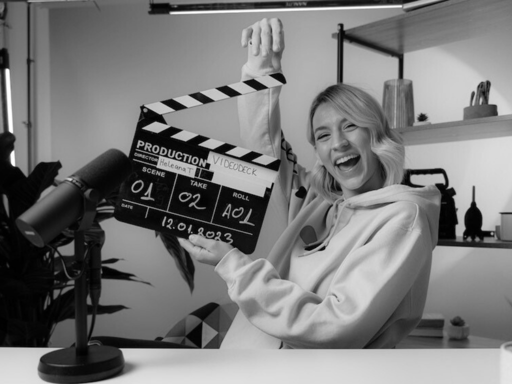 youtube starthilfe videodreh sw EIne blonde junge Frau hält eine Film-Klappe in den Händen und freut sich auf die Aufnahme.